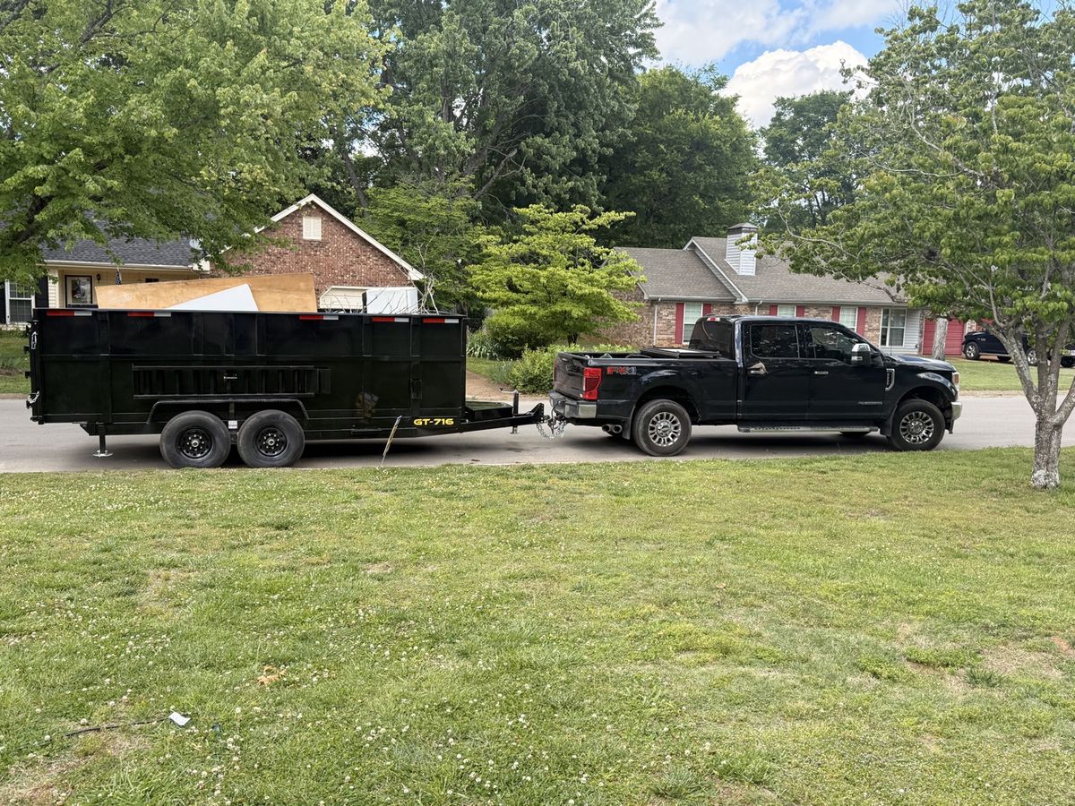 Affordable Junk Removal's black Ford truck hitched to a loaded black dump trailer on a residential street in Middle Tennessee