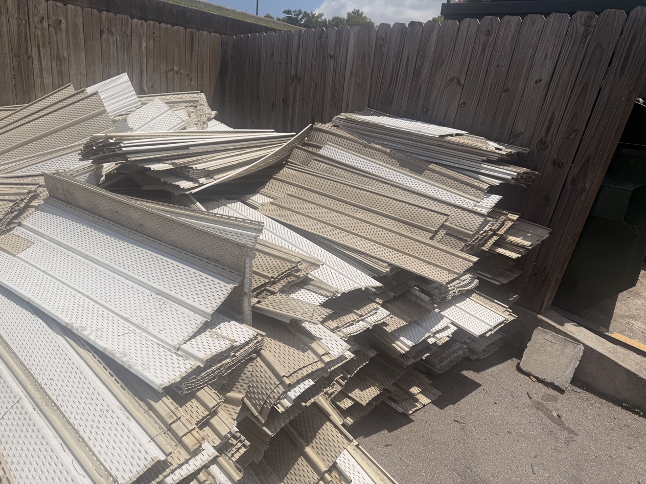 Before: pile of torn-off vinyl siding and soffit panels stacked against a wooden fence